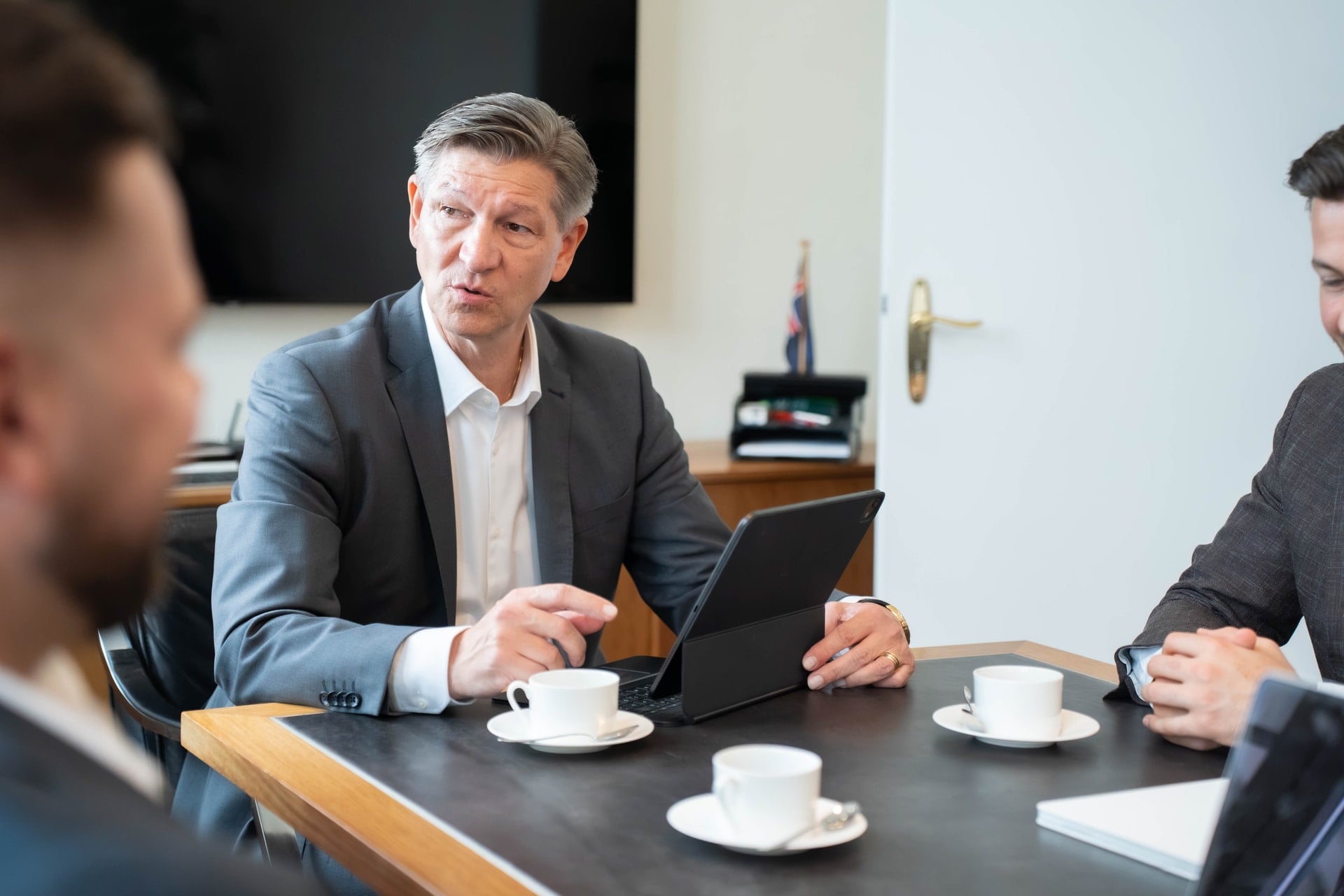 Besprechung am Tisch: Ein Kollege erläutert Unterlagen am Tablet